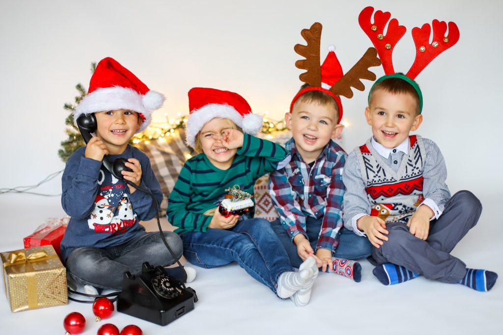 Czworo przedszkolaków w radosnym, świątecznym nastroju pozuje w czapkach świętego mikołaja i rogach renifera