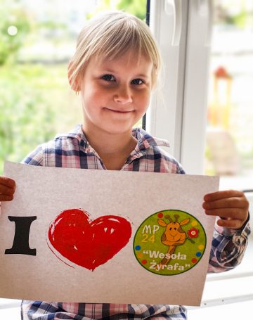 Zdjęcie uśmiechniętej dziewczynki - przedszkolaka trzymającej kartkę z napisem I love MP23