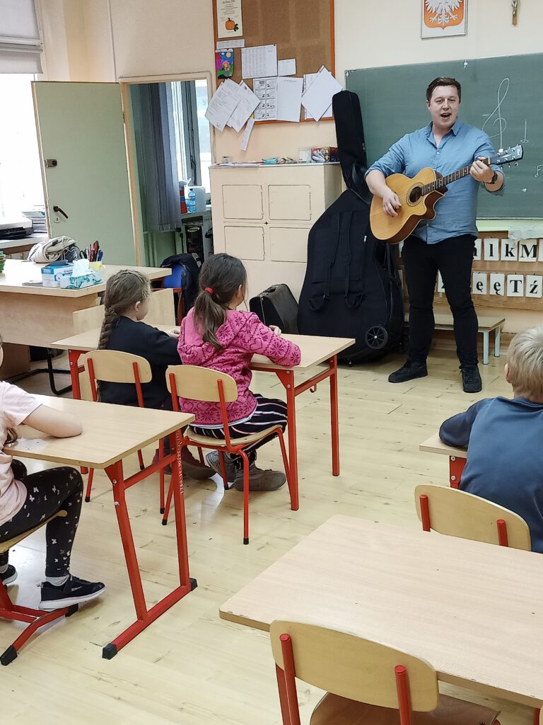 Pan Michał Nienadowski grający na gitarze przed uczniami