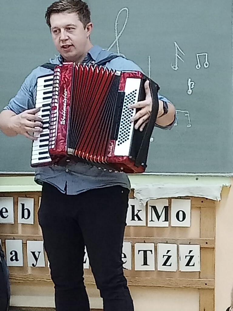 Pan Michał Nienadowski grający na harmonii przed uczniami