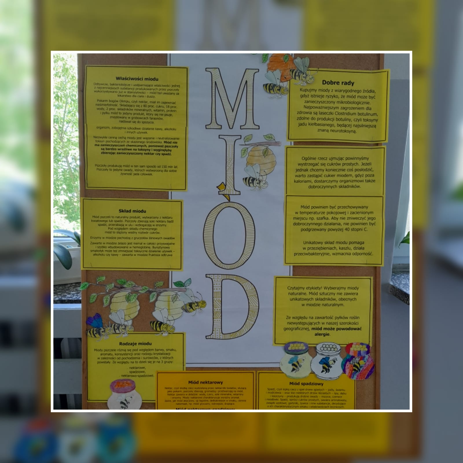 przygotowany przez uczniów plakat informacyjnym w zaletach miodu - duża tablica z żółtymi kartkami, kolorowe pszczoły i dzbanki z miodem