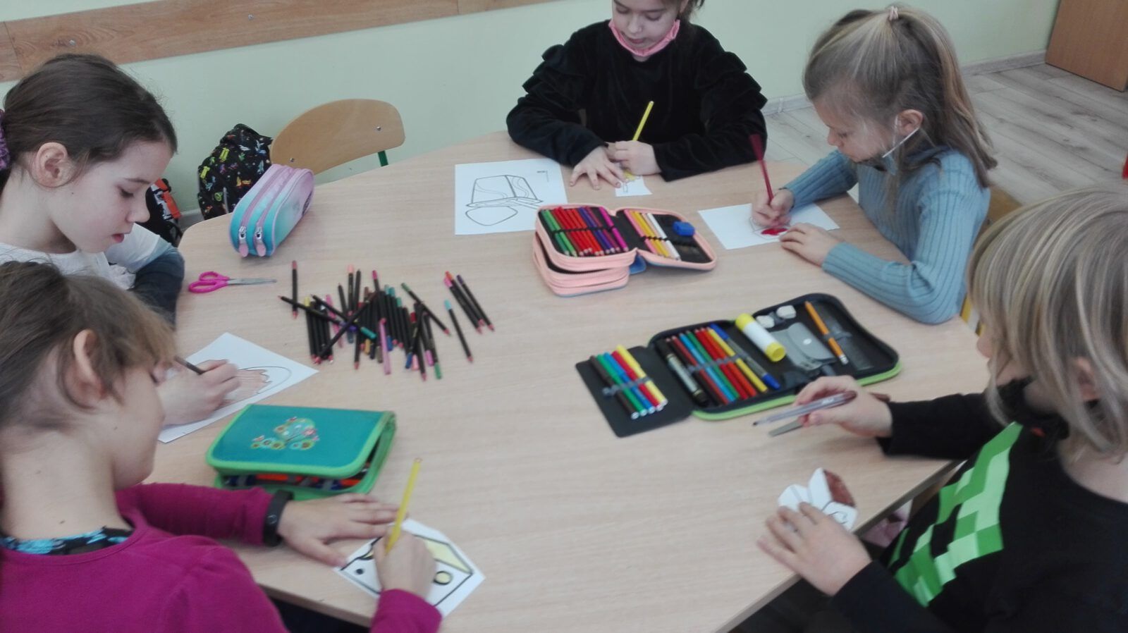 uczniowie siedzą przy stole i rysują swoje prace plastyczne