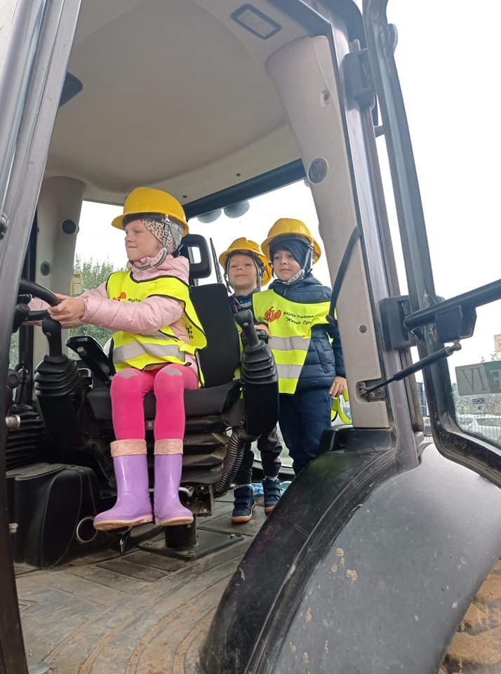 Dzieci w traktorze w kaskach. Dziewczynka siedzi za kierownicą traktora