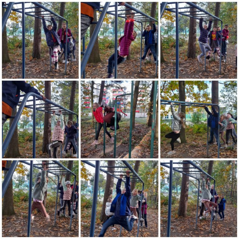 Uczniowie w przyszkolnym lesie bawią się na placu zabaw, np. wiszą do góry nogami i na rękach na metalowych drabinach