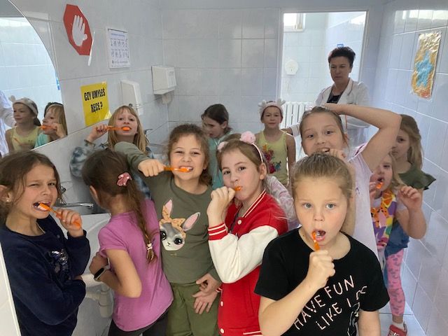 dzieci w łazience szkolnej myją zęby fluorem w towarzystwie pielęgniarki szkolnej