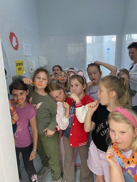 dzieci w łazience szkolnej myją zęby fluorem w towarzystwie pielęgniarki szkolnej