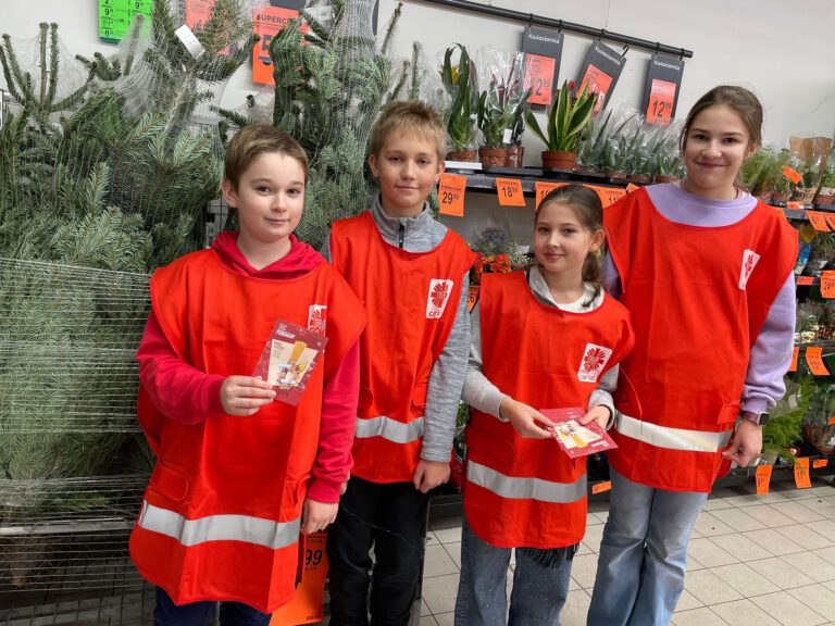 2 dziewczynki i 2 chłopców na tle choinek, w czerwonych strojach wolontariuszy
