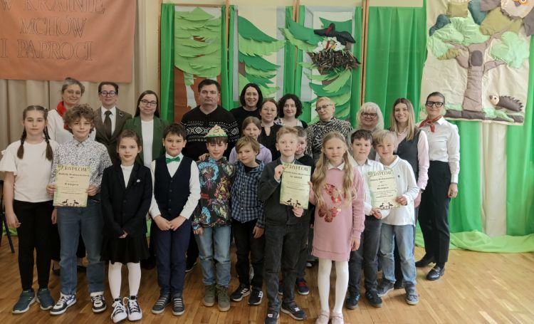 grupa uczniów i nauczycieli na tle dekoracji lasu